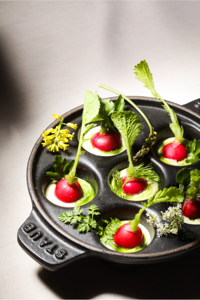 A dish with radishes and herbs arranged in a cast iron pan.