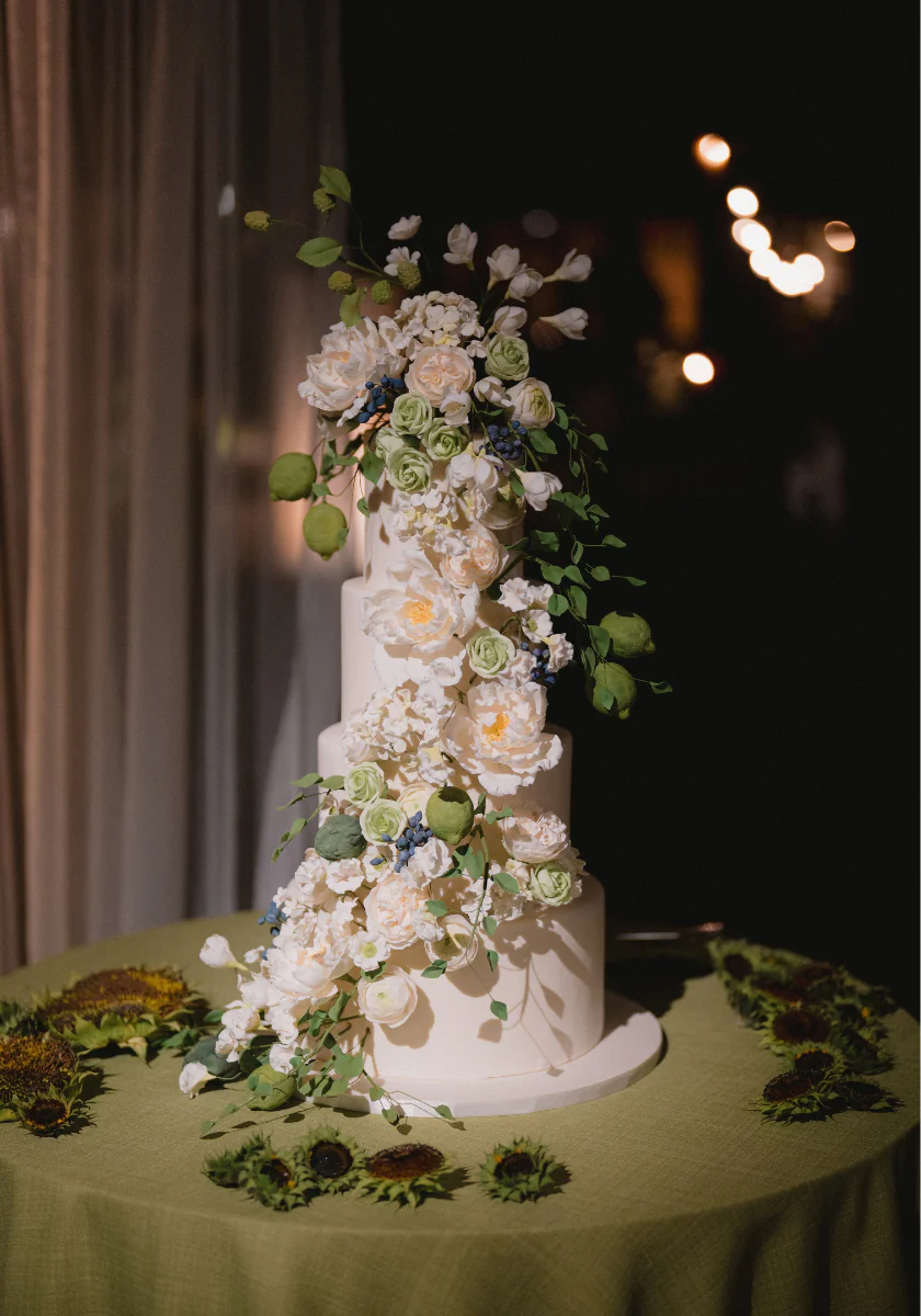 A four-tiered white wedding cake decorated with an elaborate cascading arrangement of white and green sugar flowers and foliage.