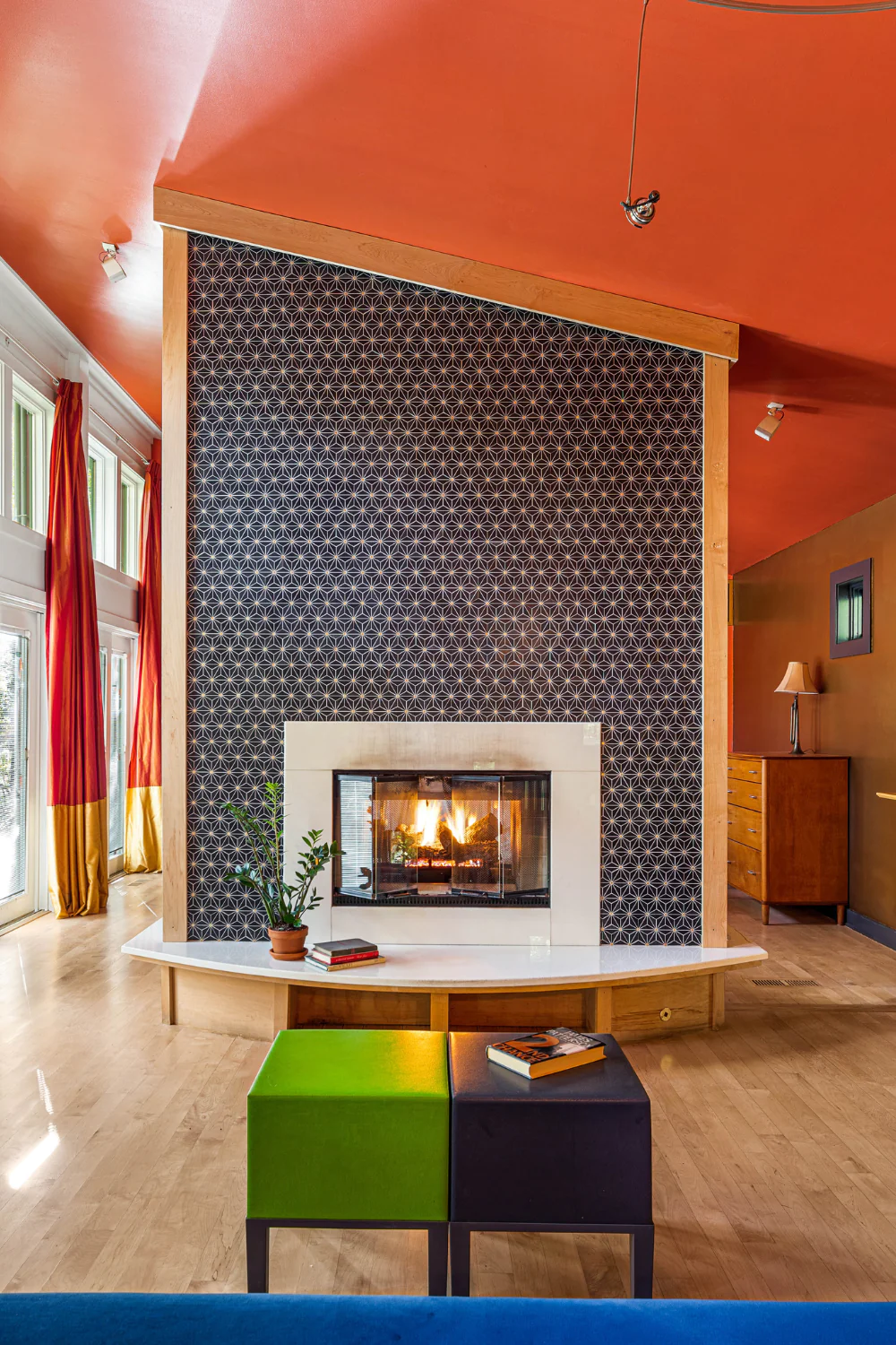 Modern living room with geometric-tile fireplace, white mantel, wood floors, colorful drapes, and bold ceilings. Contemporary and inviting.