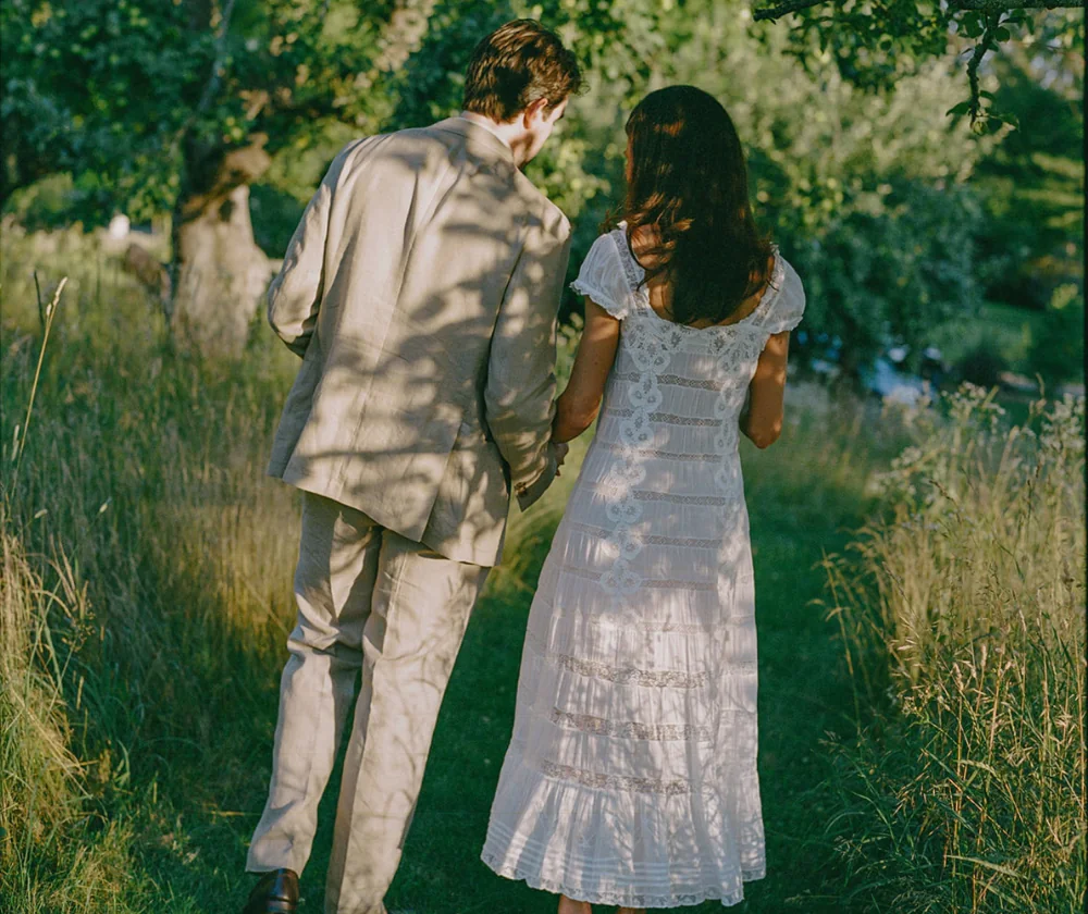 A couple walking hand in hand through a grassy meadow.